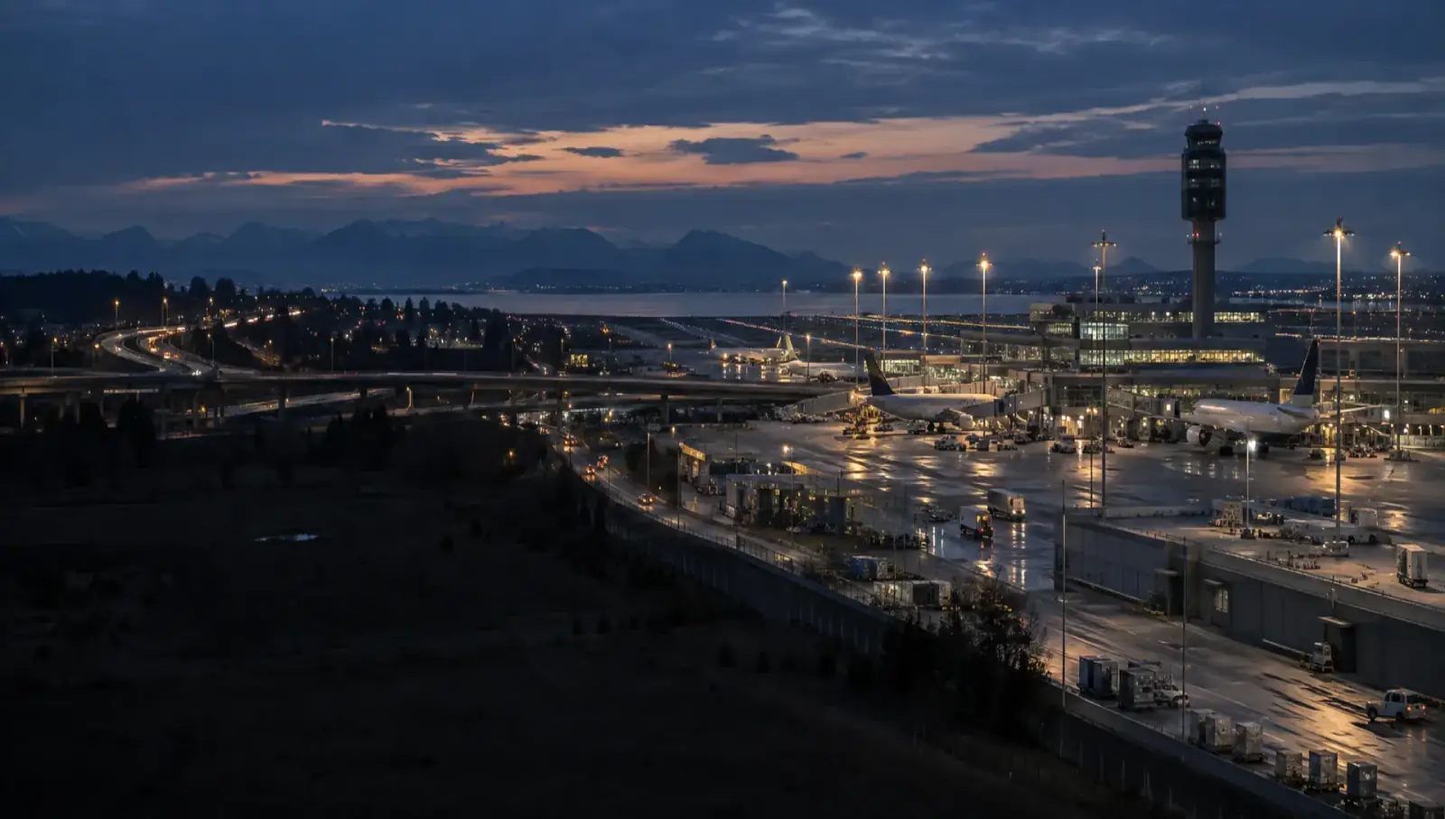 Vista nocturna de una infraestructura aeroportuaria pública con plataformas y torre de control.